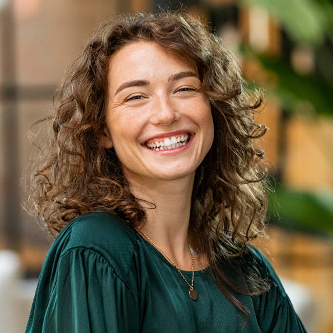Portrait of young smiling woman looking at camera with crossed arms. Happy girl standing in creative office. Successful businesswoman standing in office with copy space.